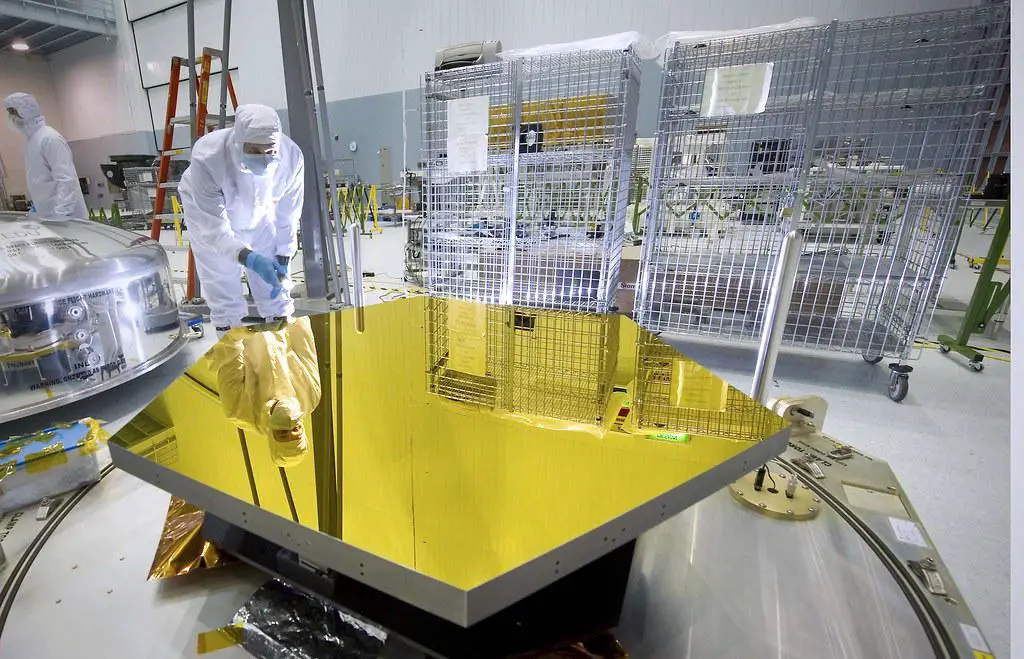 A single hexagonal beryllium mirror segment for the James Webb Space Telescope, coated in gold, reflecting a technician's image