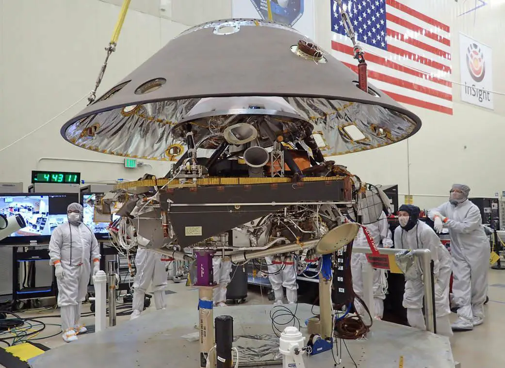 An illustration of scientific instruments, such as NASA's InSight lander and its RISE instrument, measuring Mars' rotation speed using radio wave signals.