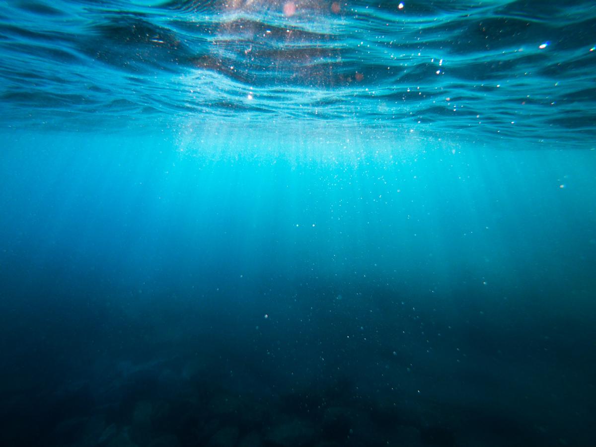 An illustration of Rayleigh scattering in the ocean, with sunlight being scattered by water molecules, predominantly in the blue wavelengths, contributing to the ocean's blue appearance.