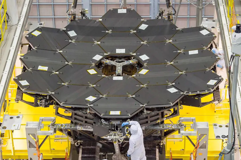 Close-up view of the James Webb Space Telescope's primary mirror segments during assembly, with technicians in clean room suits working on the structure